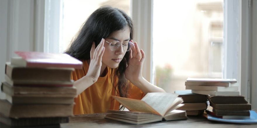 ragazza seduta davanti a una pila di libri con la testa fra le mani