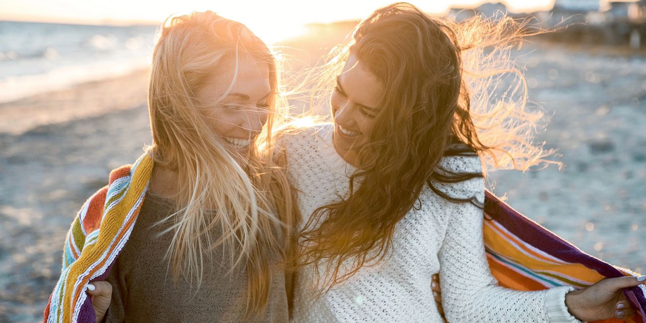 due donne sorridenti camminano sulla spiaggia al tramonto